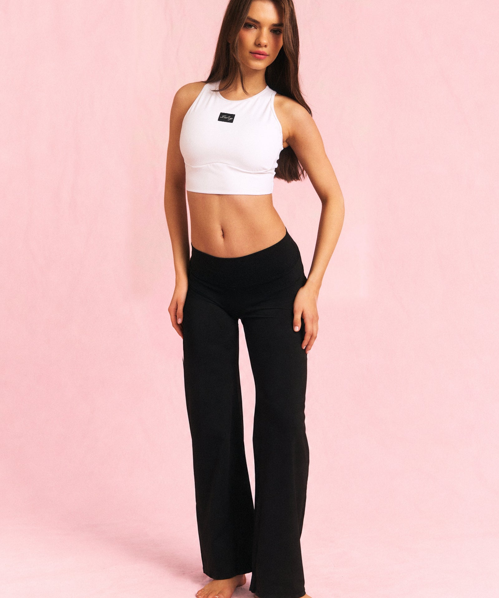 Erle i Cut out treningstopp hvit og Straight pants svart i Short, hele treningssettet på rosa bakgrunn.