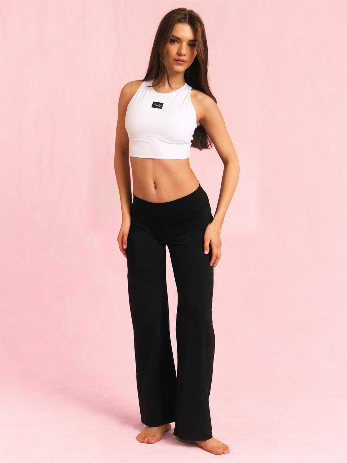 Erle i Cut out treningstopp hvit og Straight pants svart i Short, hele treningssettet på rosa bakgrunn.
